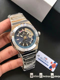 Silver wristwatch held by a hand with a visible brand tag on a dark background