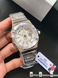 Silver wristwatch held by a hand with a visible brand tag on a dark surface