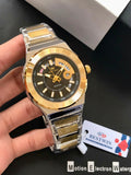 Gold and silver watch held by a hand with a visible brand tag on a dark background