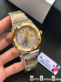 Gold and silver watch held by a hand with a visible brand tag in the background.