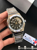 Silver watch with black face held by a hand, brand tag visible