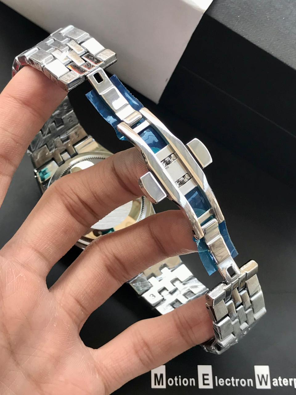 Metallic watch strap being held by a hand with a dark background